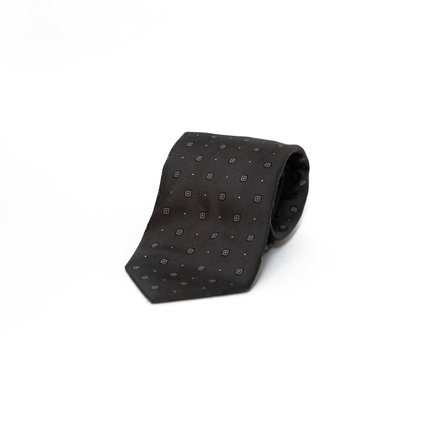 Vintage silkeslips fra Bevilacqua i dyp sort, dekorert med små grå rombemotiv og diskrete prikker spredt jevnt over hele lengden. Den fine diagonale vevingen i silken gir overflaten et subtilt glans, og det tonefattige mønsteret skaper et stramt og elegant uttrykk.