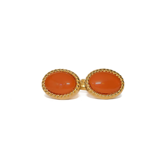 Vintage mansjettknapper fra 60-tallet med oval cabochon-slipt sten i varm oransje, innrammet av en tvunnet gullkant som gir et fint dekorativt preg. Stenens glatte og polerte overflate står i kontrast til den strukturerte rammen og gir et levende detaljspill. Et karakterfullt valg for mannen som ønsker å sette en farget aksent til skjorten.