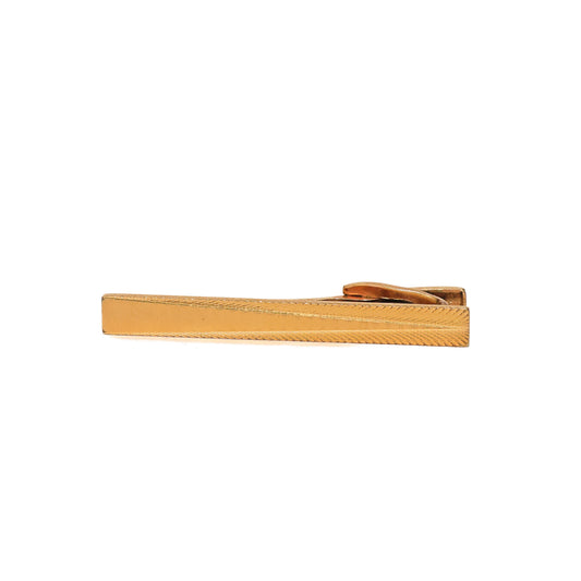 Vintage slipsnål fra 60-tallet i avlang form og gulltone. Fint riflede felt strekker seg skrått langs over- og underkant og rammer inn et glatt, polert midtfelt. Det enkle, men distinkte uttrykket gir slipsnålen et raffinert preg uten å bli for prangende. Et tidløst valg for mannen som setter pris på rene linjer og diskret eleganse.
