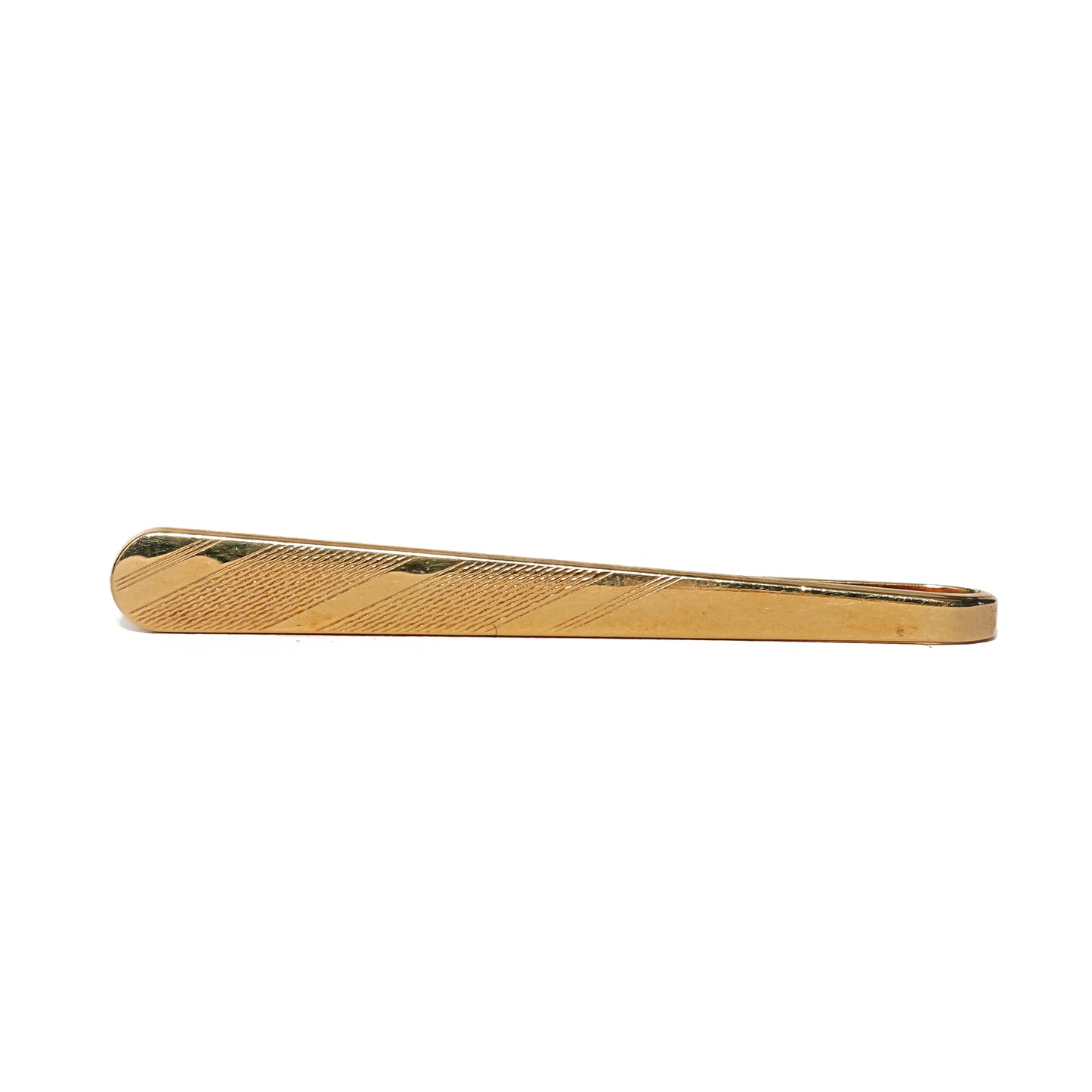 Vintage slipsnål fra 70-tallet i avlang form og gulltone. Et midtfelt med fine, diagonale linjer brytes opp av polerte striper som skjærer over mønsteret, og kontrasten mellom det matte og det blanke gir et grafisk og dynamisk uttrykk. Den slanke formen og de rene detaljene gir slipsnålen et moderne preg. Et stilrent valg for mannen som setter pris på diskrete linjer og tidens designspråk.