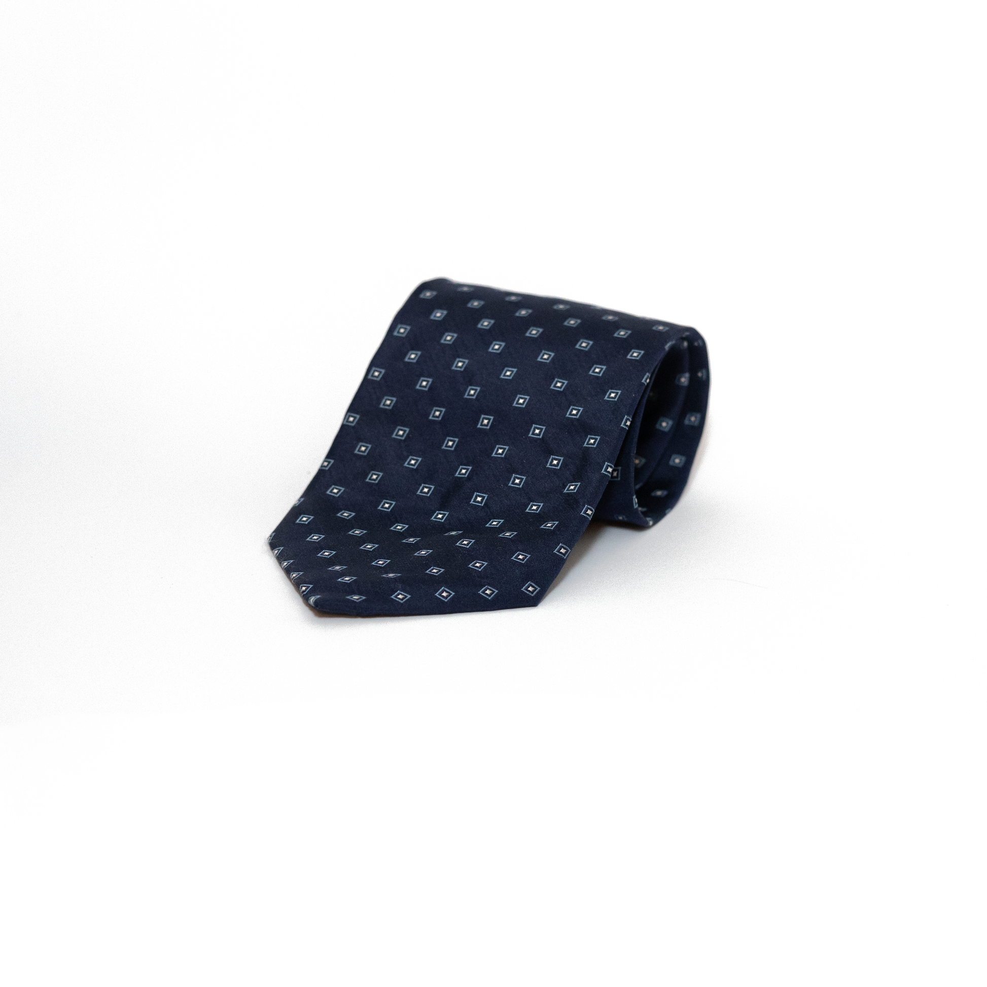 Mørkeblått vintage slips med et diskret geometrisk mønster i små firkanter i sølvtone. Mønsteret gir slipset dybde og variasjon, samtidig som det holder seg innenfor et klassisk og dempet uttrykk.