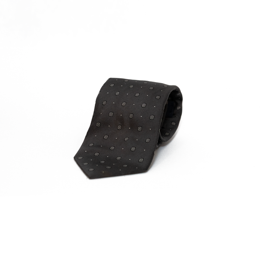 Vintage silkeslips fra Bevilacqua i dyp sort, dekorert med små grå rombemotiv og diskrete prikker spredt jevnt over hele lengden. Den fine diagonale vevingen i silken gir overflaten et subtilt glans, og det tonefattige mønsteret skaper et stramt og elegant uttrykk.
