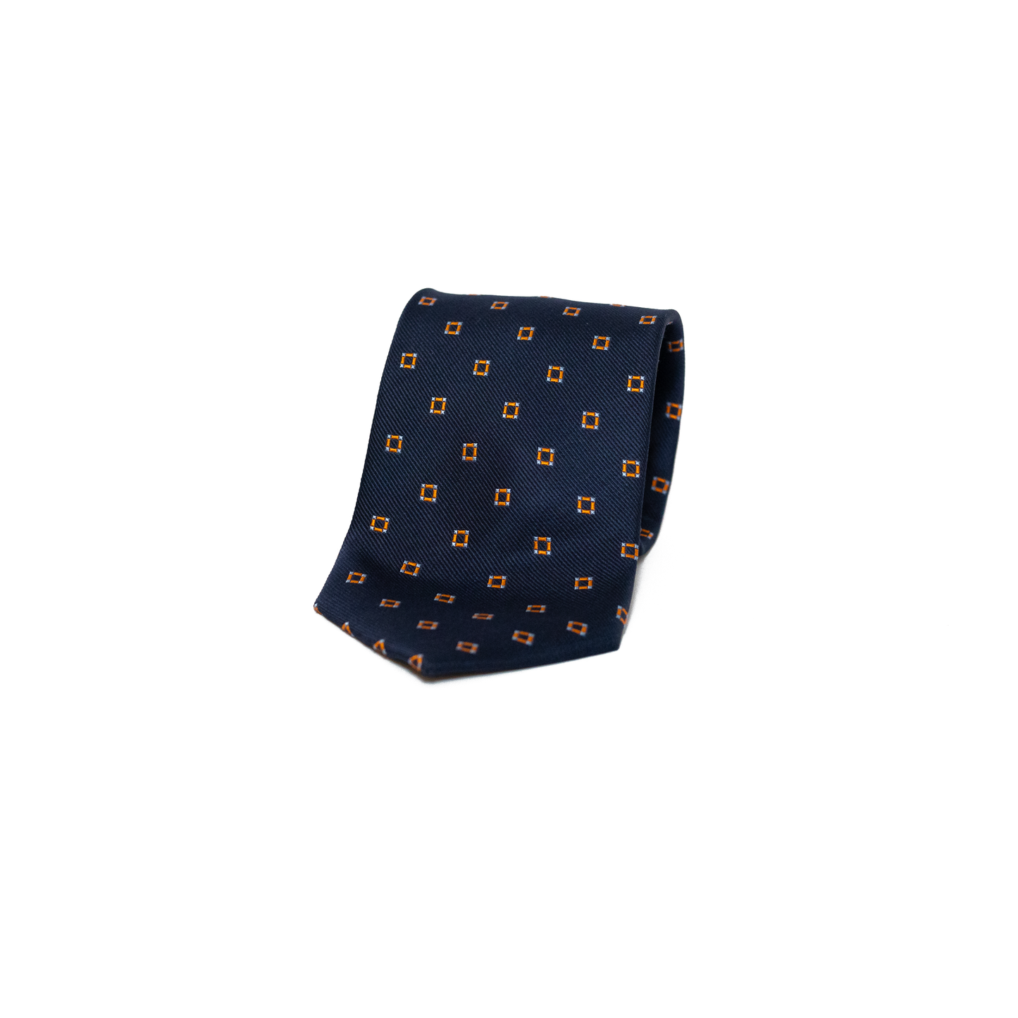 Vintage silkeslips fra Belmonte i dyp marineblå, dekorert med små oransje romber spredt jevnt over hele lengden. Den fine diagonale vevingen i silken gir overflaten et subtilt glans, og kontrasten mellom det rolige blå og de varme oransje detaljene skaper et levende, men dempet uttrykk. Et stilsikkert valg som kler både dressen og den mer uformelle blazeren.