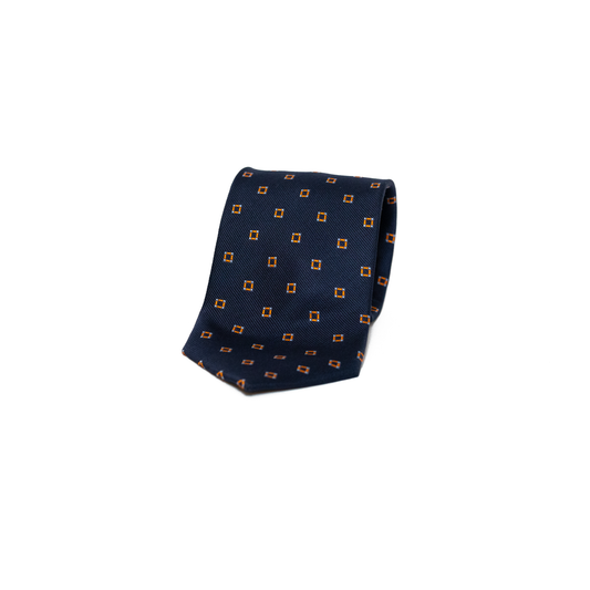 Vintage silkeslips fra Belmonte i dyp marineblå, dekorert med små oransje romber spredt jevnt over hele lengden. Den fine diagonale vevingen i silken gir overflaten et subtilt glans, og kontrasten mellom det rolige blå og de varme oransje detaljene skaper et levende, men dempet uttrykk. Et stilsikkert valg som kler både dressen og den mer uformelle blazeren.