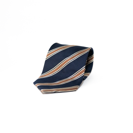 Mørkeblått vintage slips fra Monsieur Gaspar Dido, med diagonale striper i kobberbrunt og tynnere striper i hvitt. Det klassiske stripemønsteret gir slipset et tradisjonelt regimentalt uttrykk, samtidig som det holder seg innenfor et dempet og tidløst utseende.