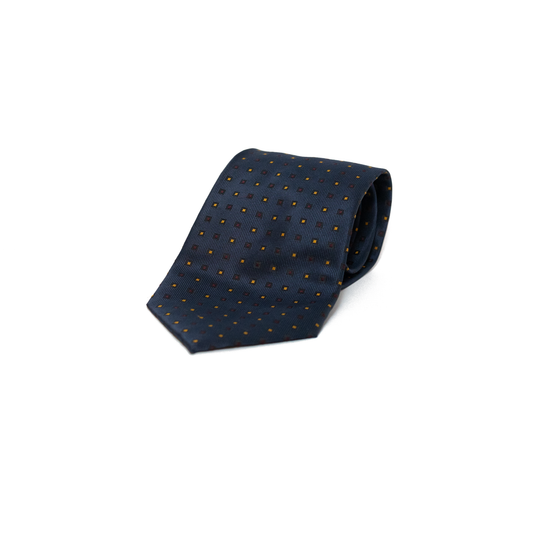 Mørkeblått vintage slips fra italienske Navigare, med et diskret geometrisk mønster i små firkanter i oransje og burgunder. Mønsteret gir slipset varme og dybde, samtidig som det holder seg innenfor et klassisk og dempet uttrykk.