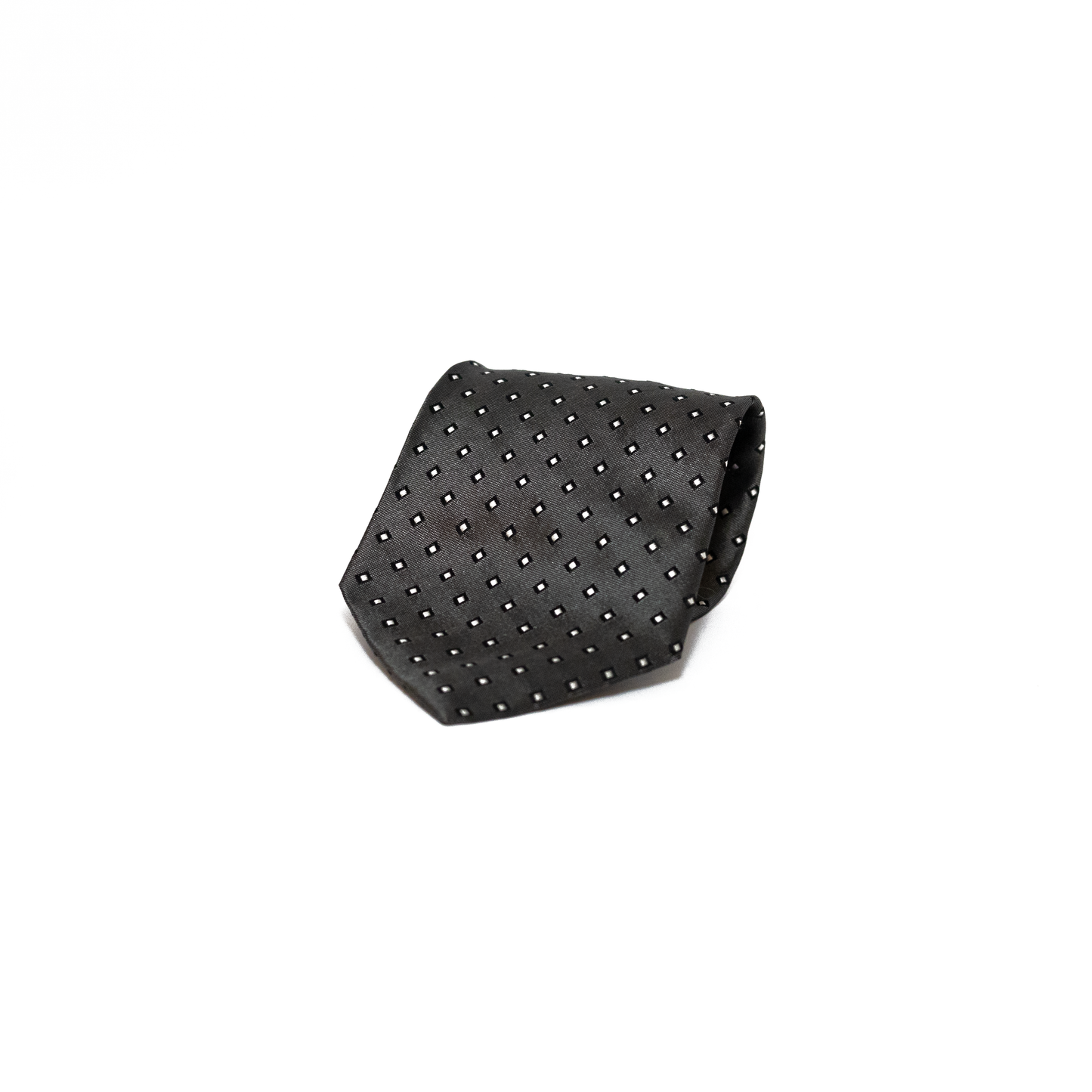Vintage silkeslips fra Trussardi i mørk antrasittgrå, dekorert med små hvite rombemotiv spredt jevnt over hele lengden. Den fine diagonale vevingen i silken gir overflaten et subtilt glans, og det rytmiske mønsteret skaper et grafisk, men dempet uttrykk.